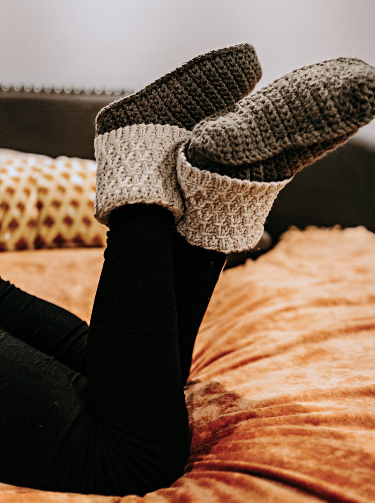 Model wearing slipper boots and leggings laying on a bed with an orange blanket.