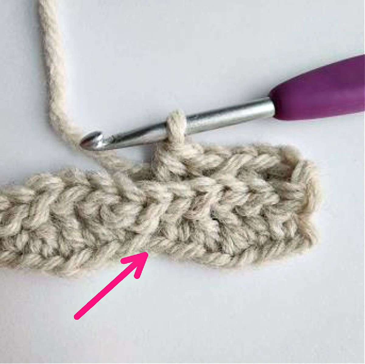 A close-up photo and pink arrow showing stitch placement of a long double crochet stitch.