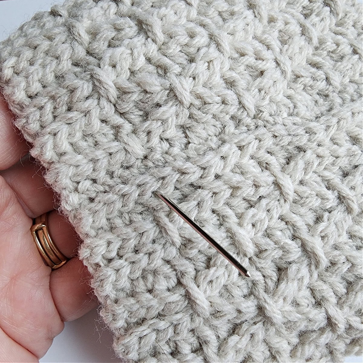 Close-up of a yarn needle showing where to work the first finishing stitch on the slipper cuff seam.