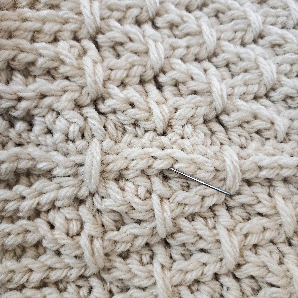 Close-up of a yarn needle creating a second set of finishing stitches along the seam of a cowl.