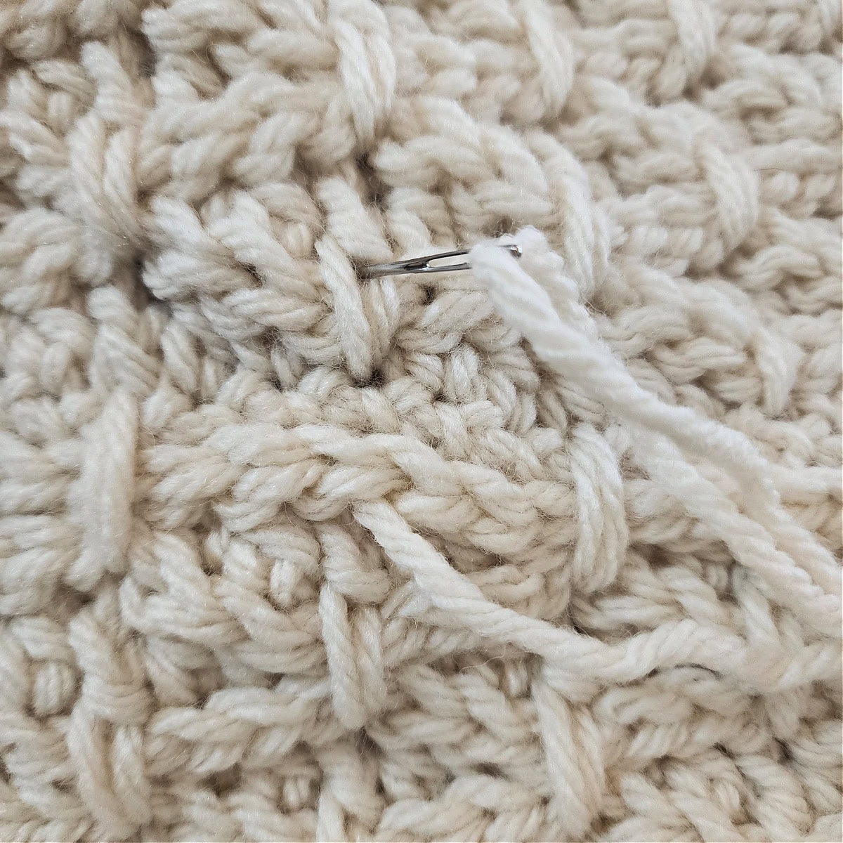 A yarn needle inserted into a double crochet stitch above the cowl seam to create a finishing stitch.