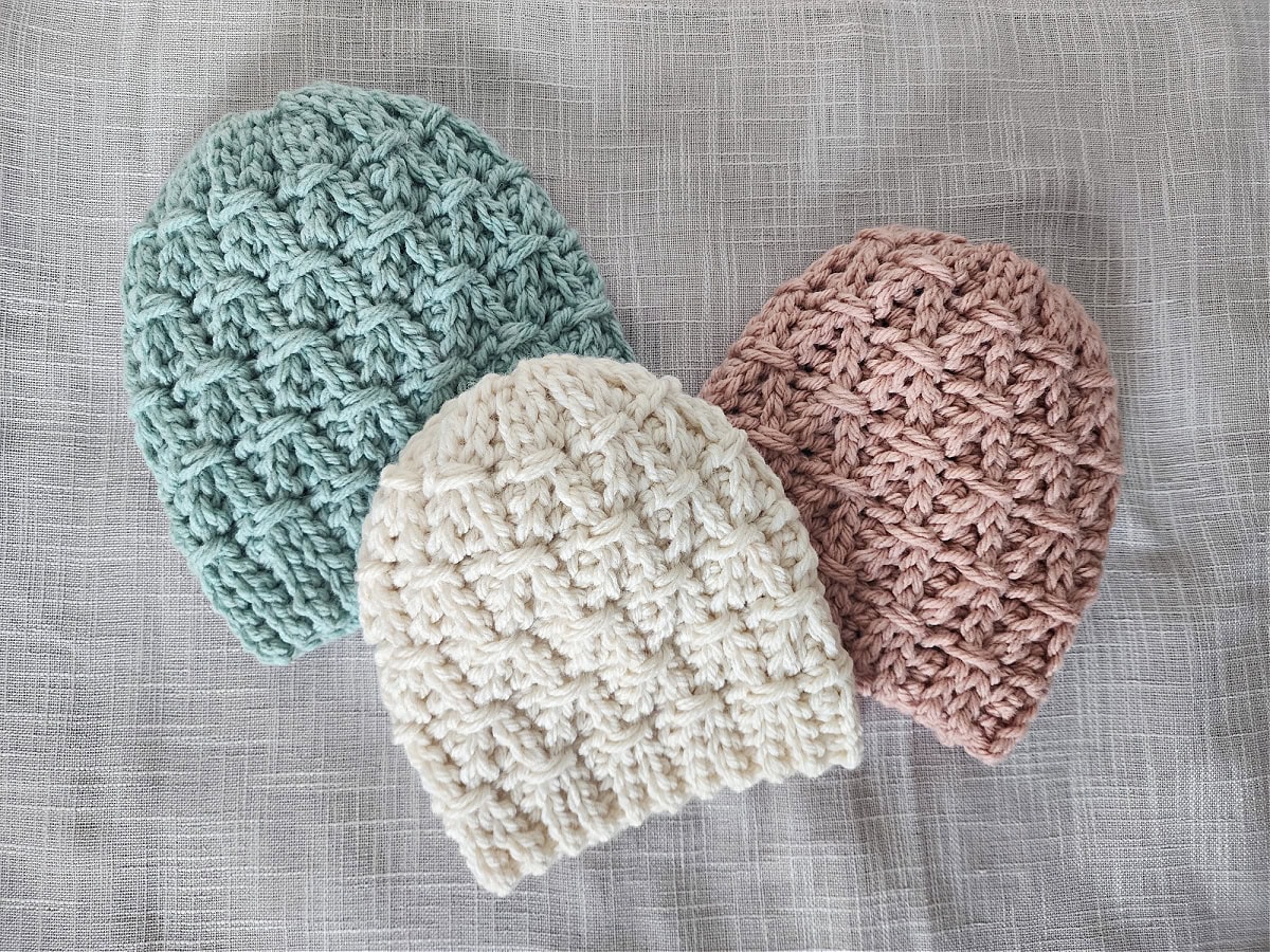 Three chunky crochet hats laying on a woven fabric.