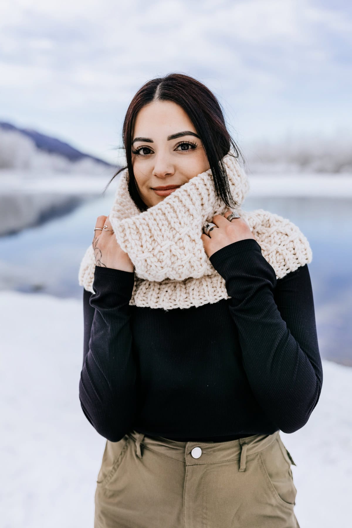 Cream color free crochet cowl pattern modeled outdoors in winter landscape.