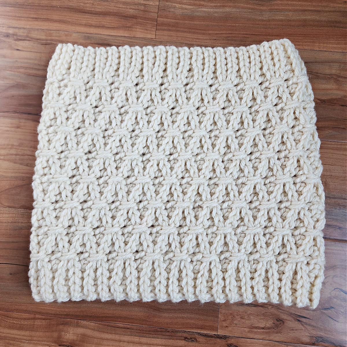 Flat lay photo of a cream colored crochet cowl in chunky yarn with a knit look crochet stitch.