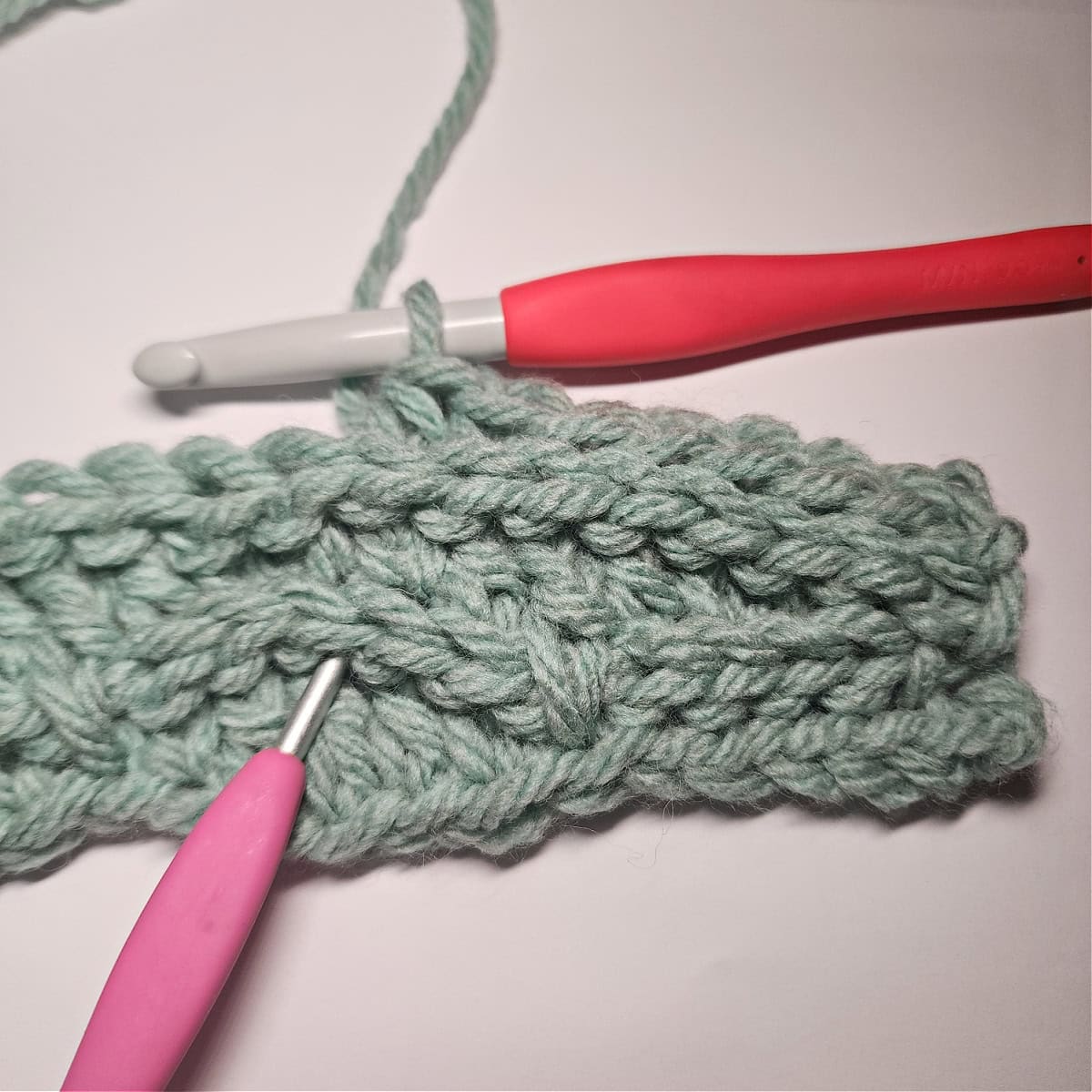 The pink crochet hook is showing where to work a double crochet from row five into a dc from 3 rows down.