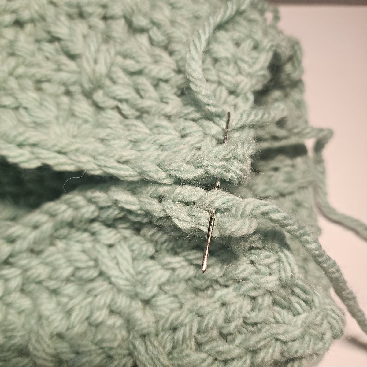 A yarn needle is showing which loops to work into to seam the crochet hat pattern.