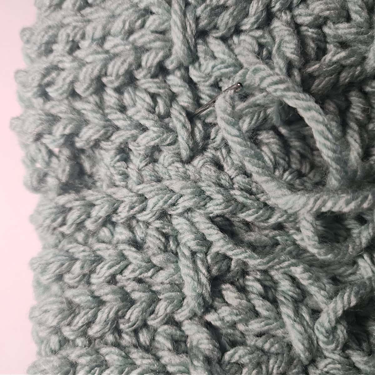 A yarn needle is showing how to work a finishing stitch to blend the seam on the crochet hat pattern.