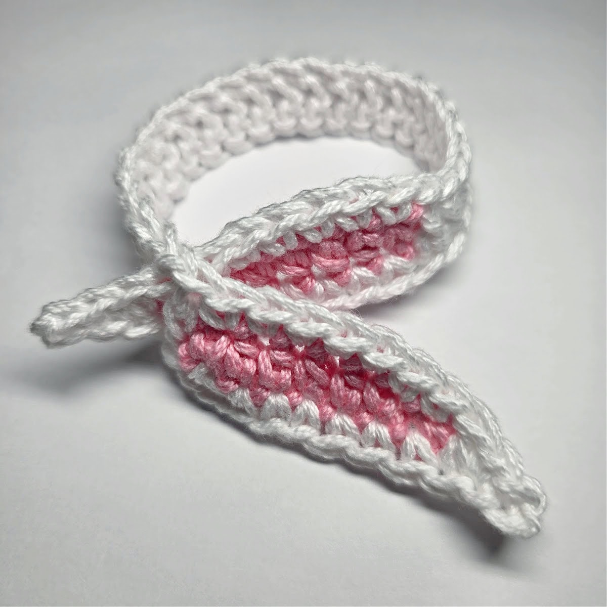 Crochet bunny ears napkin rings white with pink inner ears laying on its side.