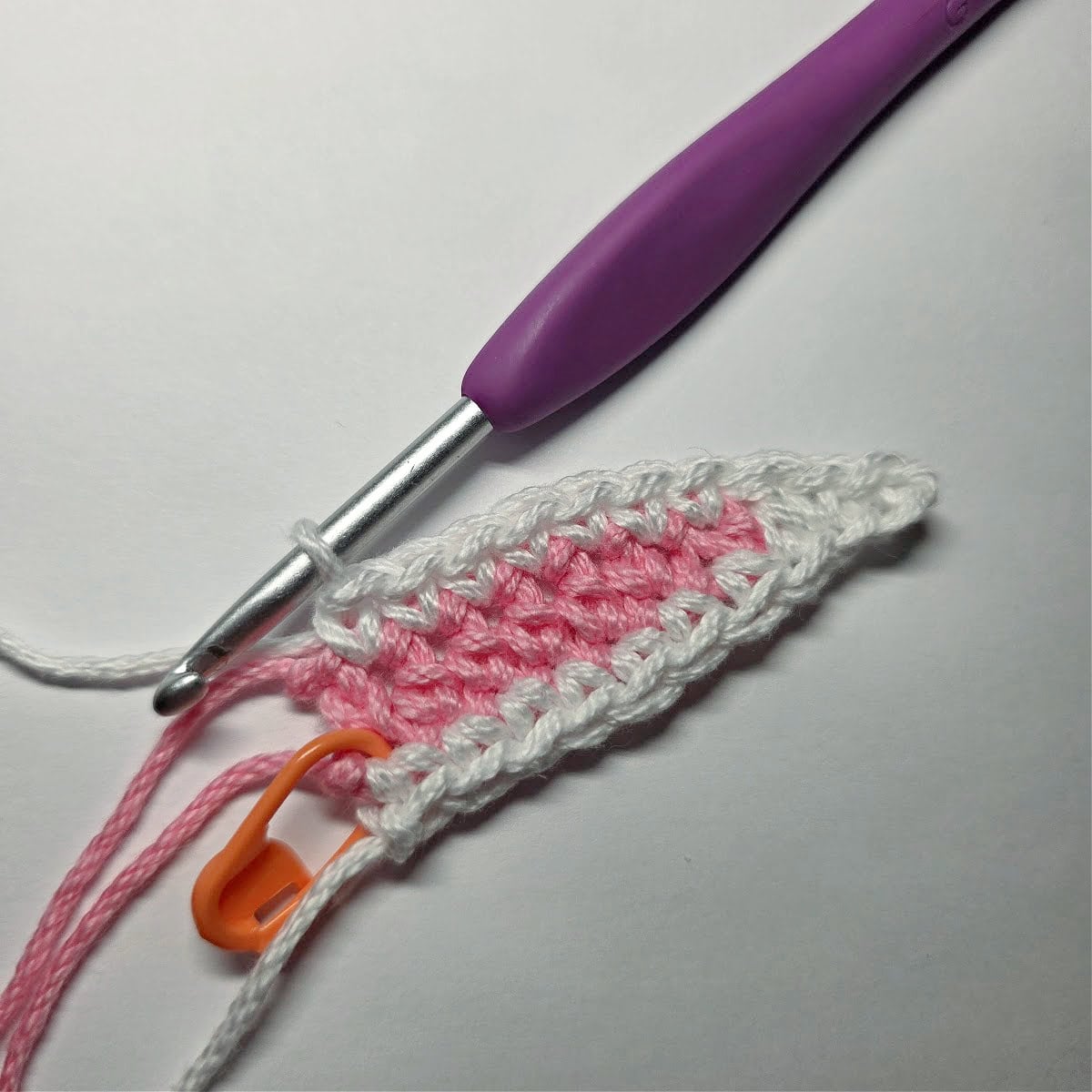 One crochet bunny ear complete with a purple crochet hook.