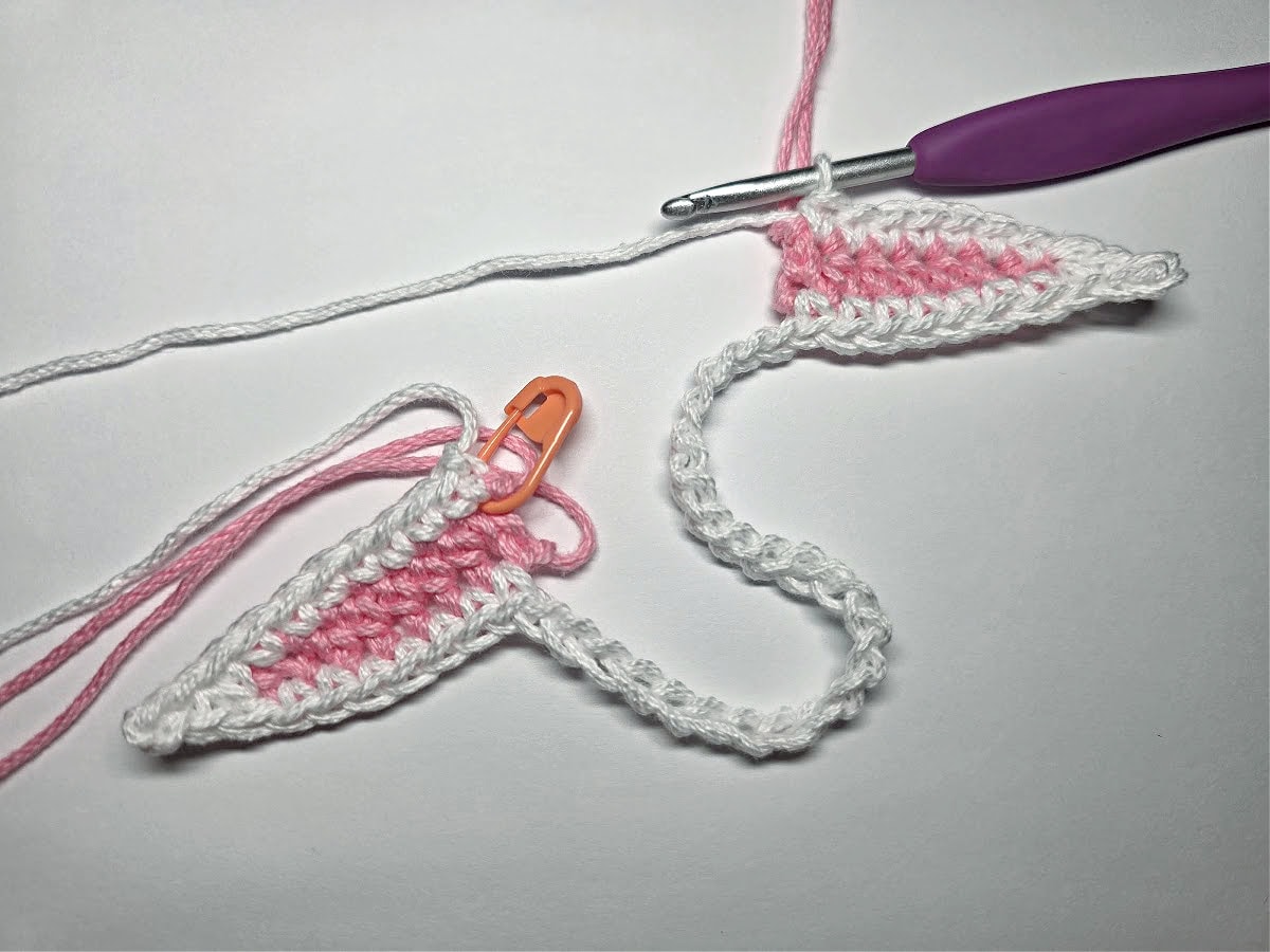 Two white and pink crochet bunny ears being connected to make a napkin ring.