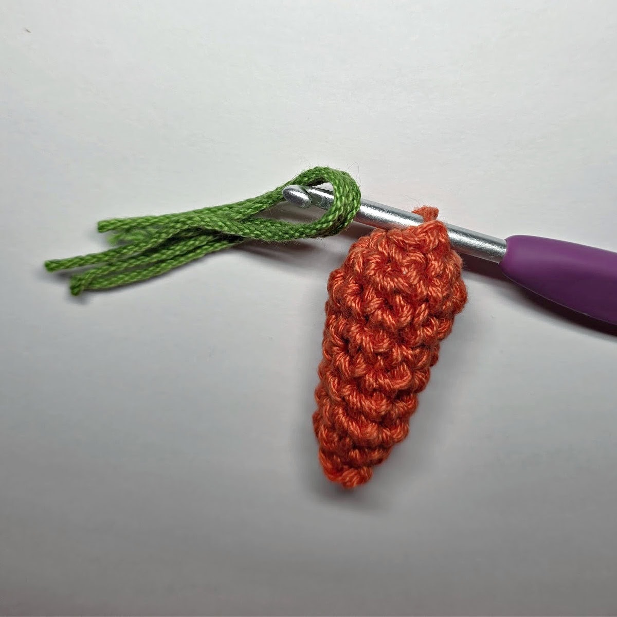 Three strands of green yarn being pulled through a stitch to create a carrot top.