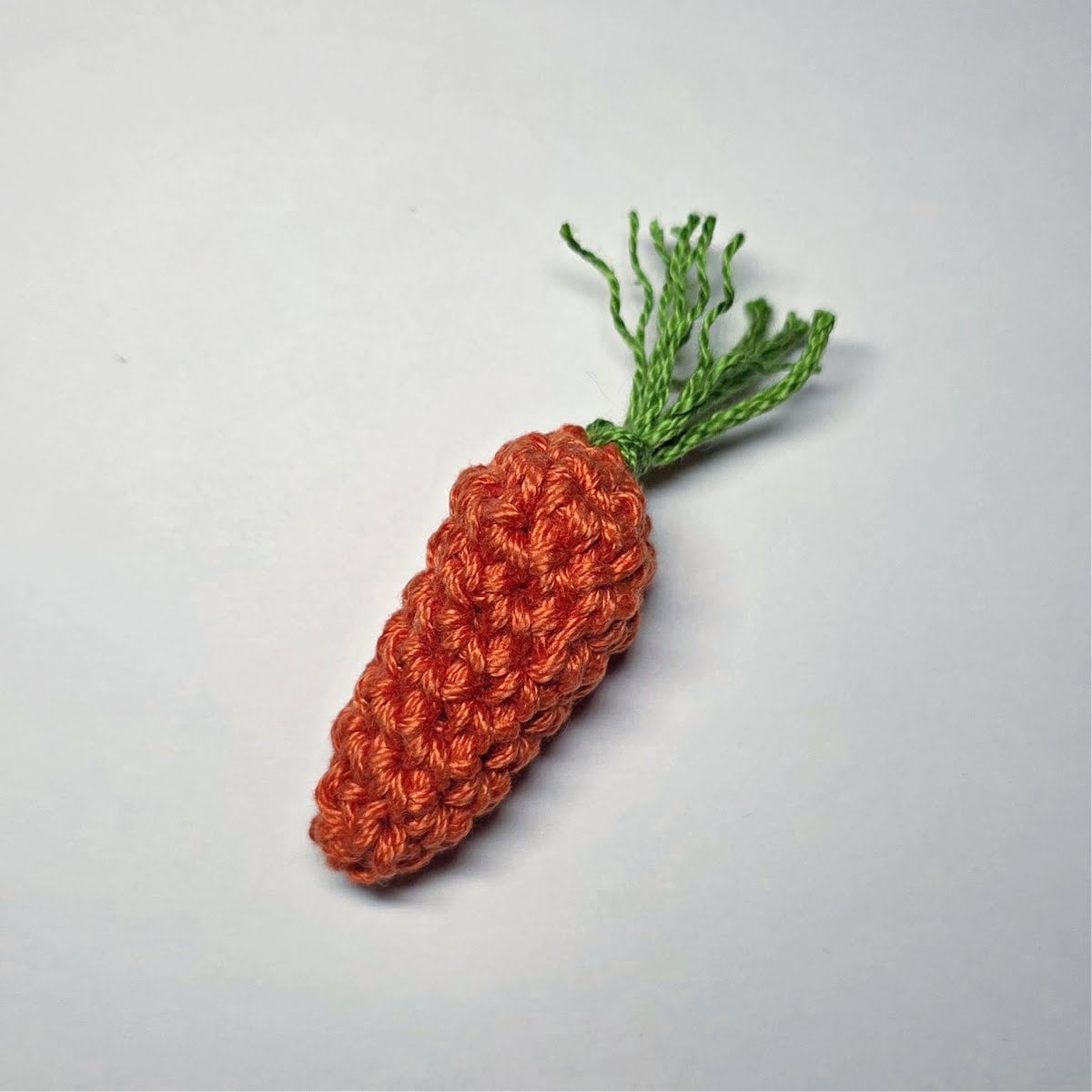 A small crochet carrot with a green carrot top.