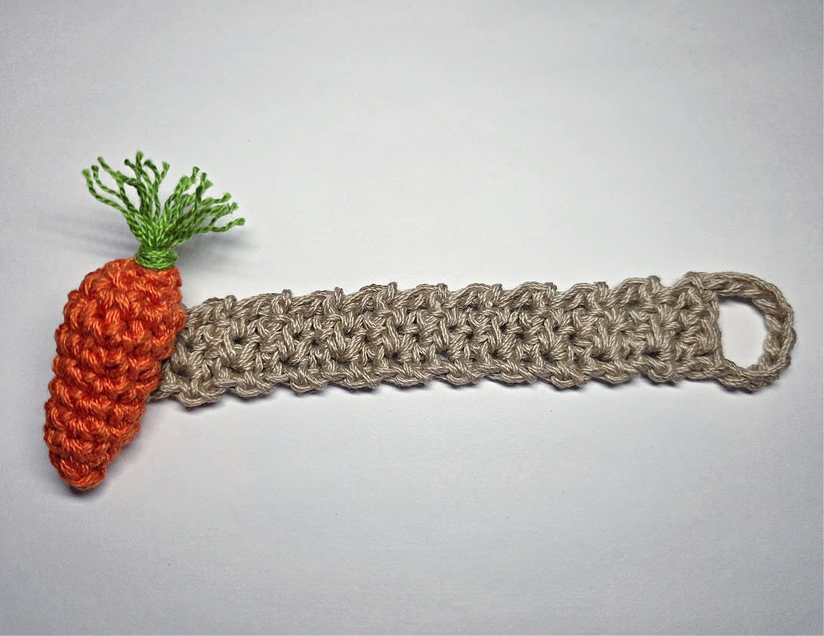 A crochet carrot attached to the end of a taupe crochet napkin holder.