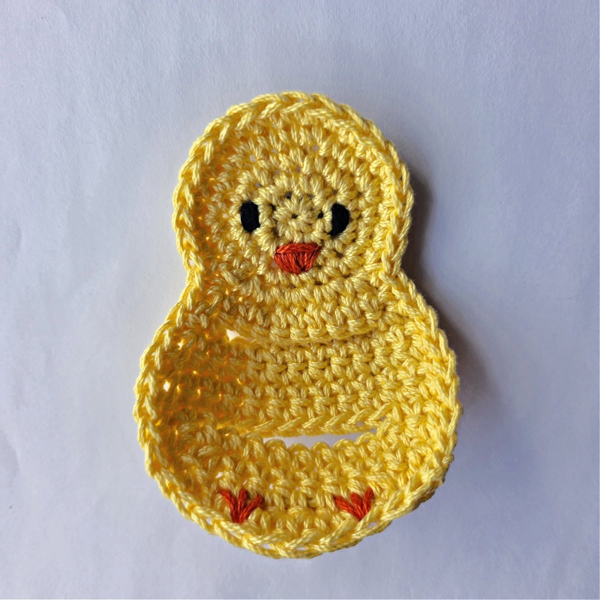 A crochet Easter chick napkin holder laying on a white background.