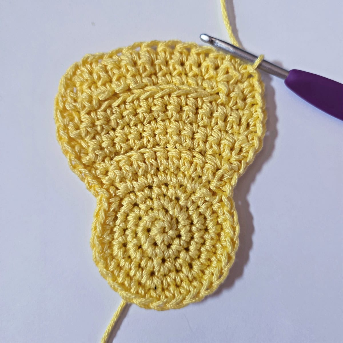 A purple crochet hook working single crochet around the perimeter of the baby chick.