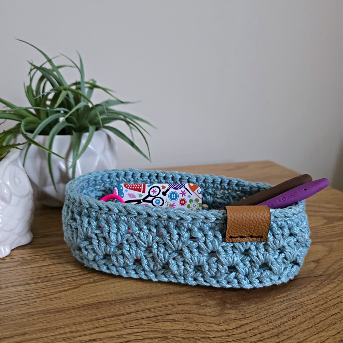 Small nightstand basket holding crochet hooks and scissors.