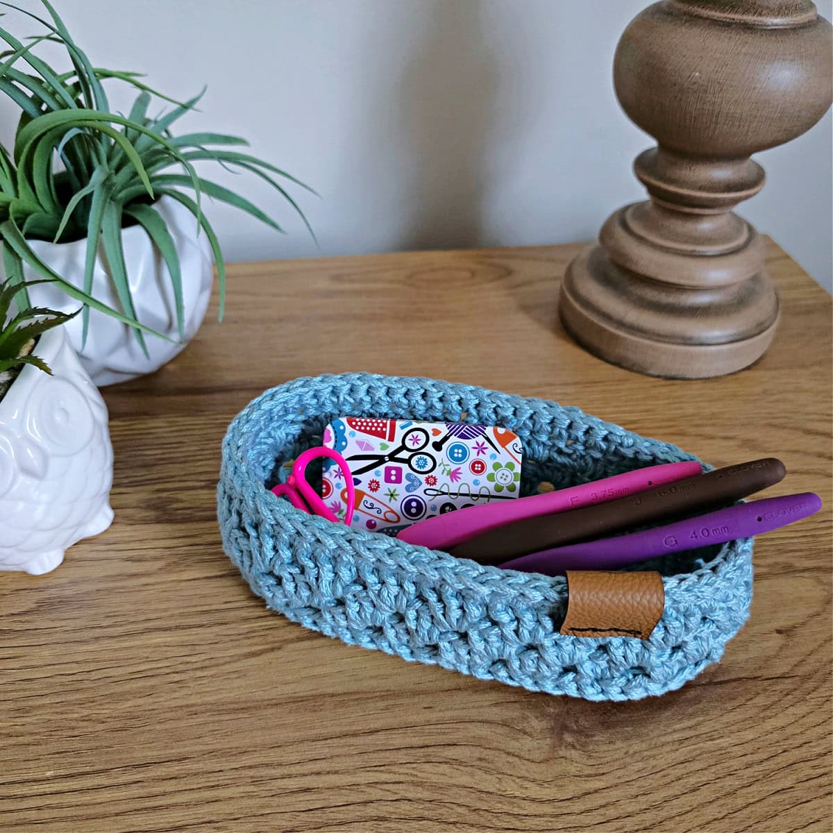 A small oval crochet basket holding crochet hooks and scissors.