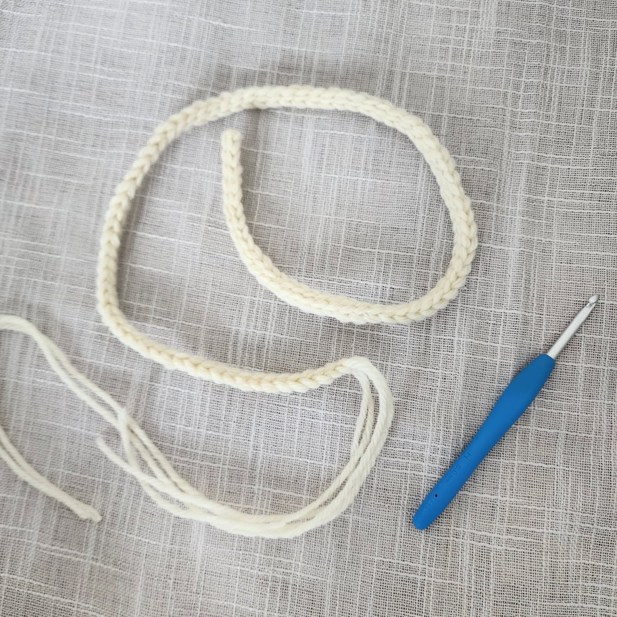 A crochet icord in cream colored yarn laying next to a blue crochet hook.