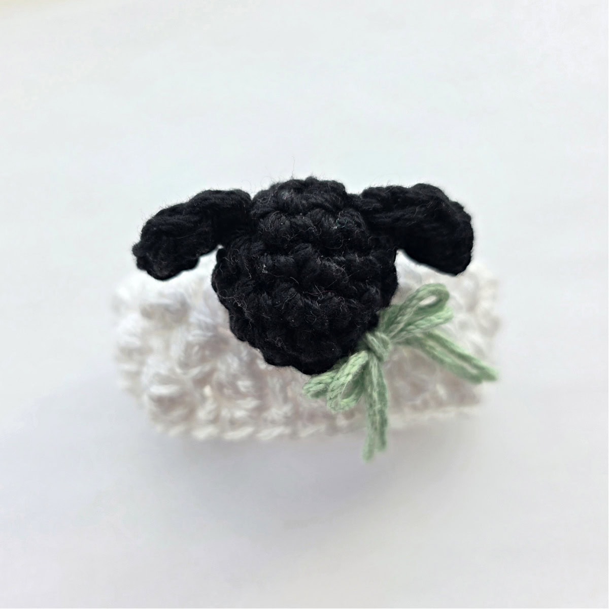 The top view of a crochet lamb napkin ring with a light green bow.