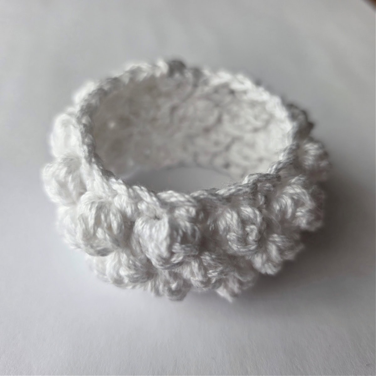 A small white crochet napkin ring with bobble stitches to create a bumpy texture.