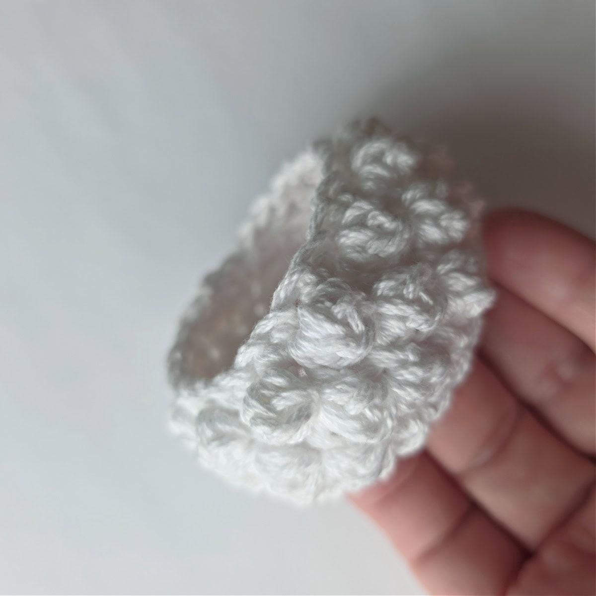 Side view of a white crochet napkin ring with bobble stitches.