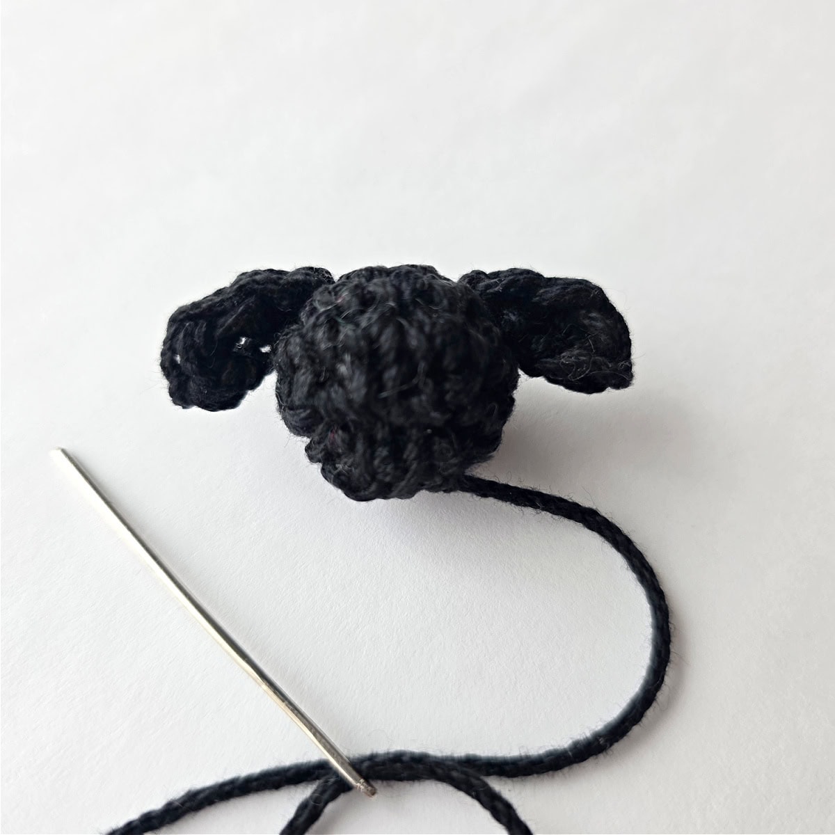 A small crocheted lamb's head with ears and a yarn needle laying next to it.