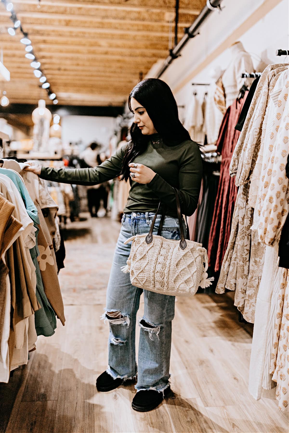 A young woman shopping for clothing carrying a cream colored crochet purse with cables and leather straps.