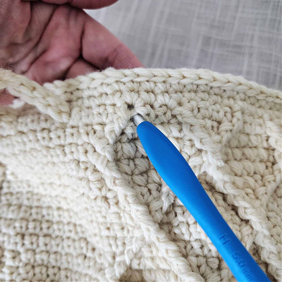 A blue crochet hook helping to pull the icord through a stitch in the bag.