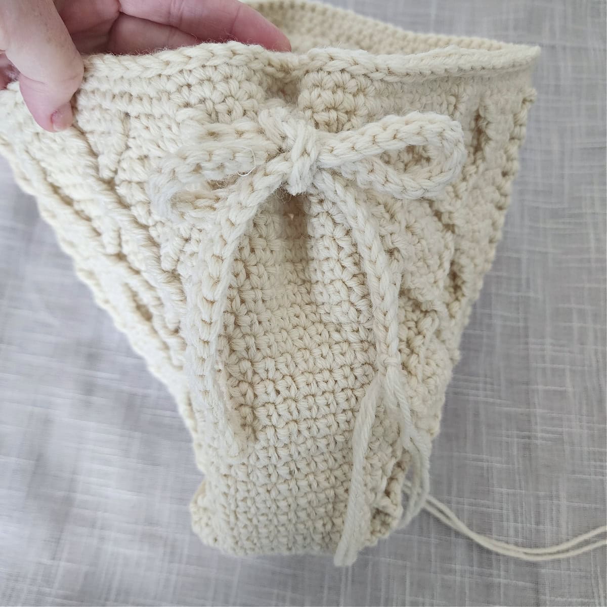 A crochet icord tied into a bow after gathering a pleat on a bag.