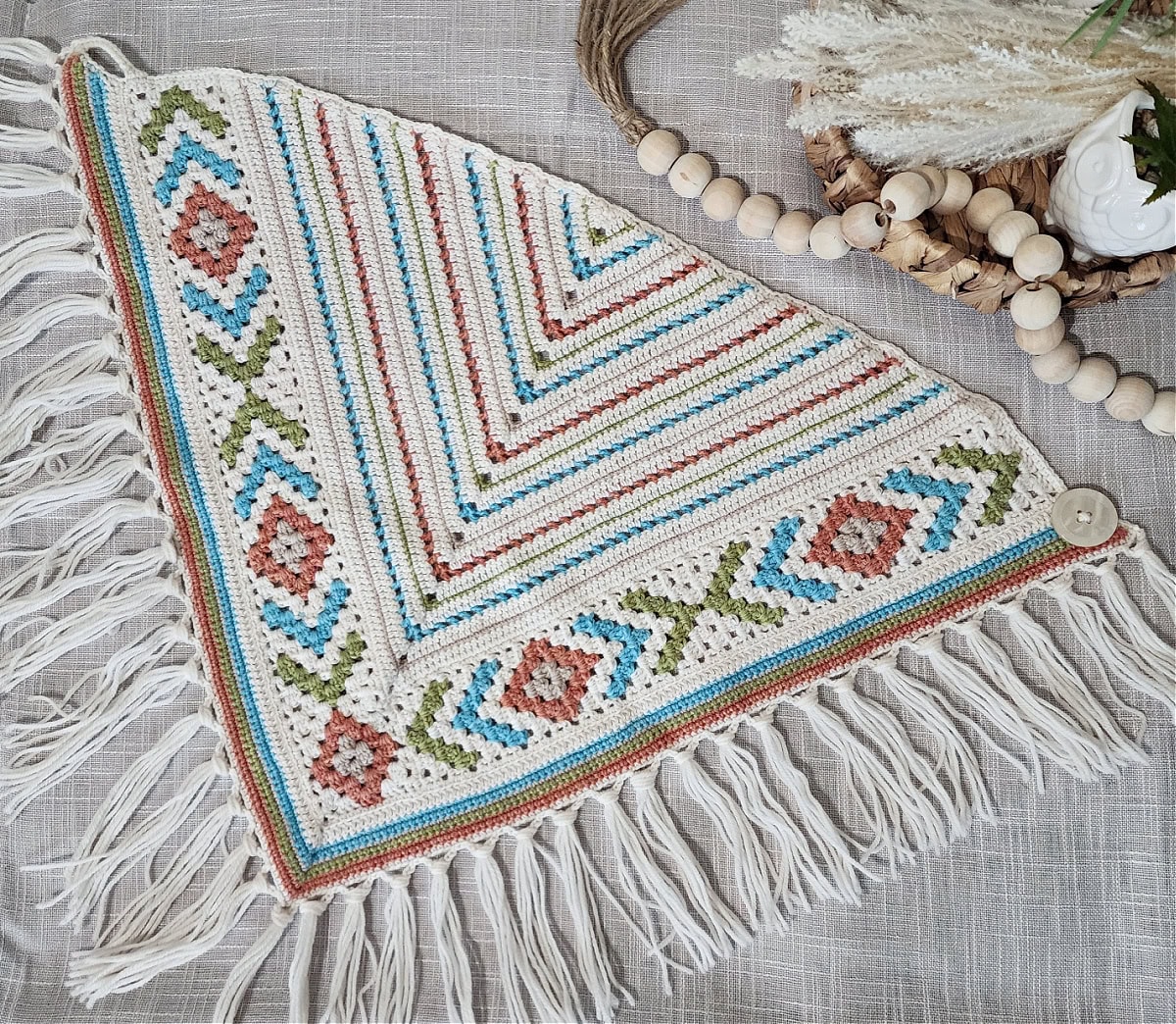 The Boho Chic Mosaic Scarf laid flat on a linen covered surface with wooden beads and a tray with small plant.