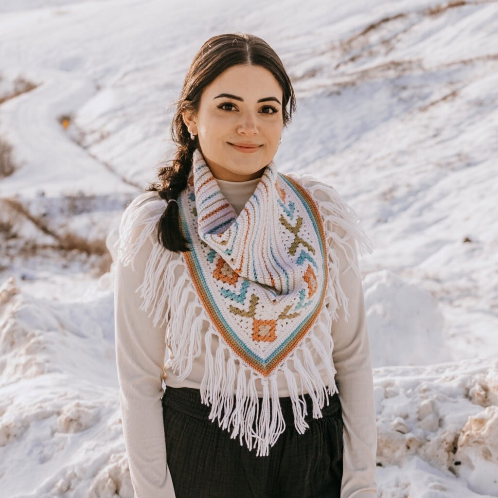 You model wearing a crochet triangular scarf pattern outside in the snow.