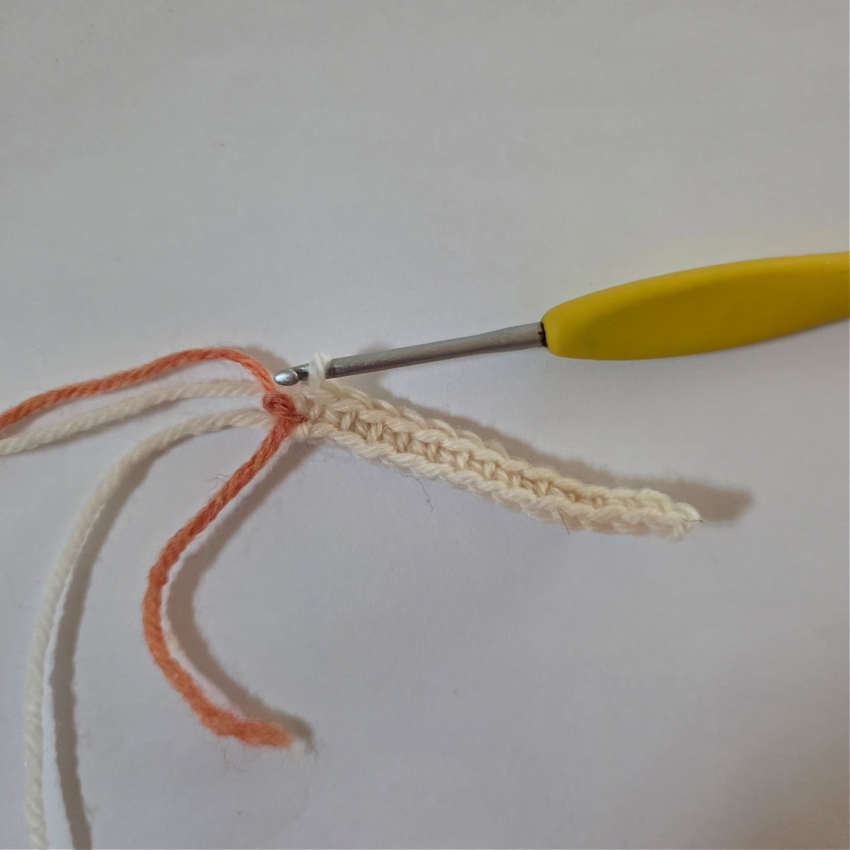 An orange scrap piece of yarn marking a stitch in a row of single crochet stitches.