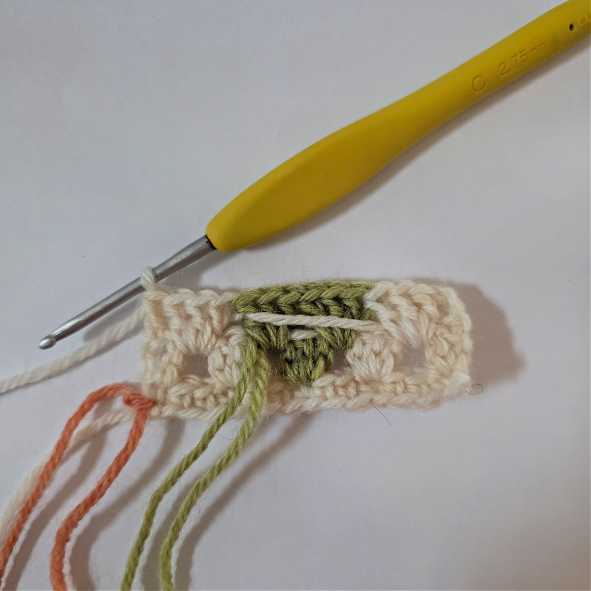 A yellow crochet hook and beginning of a swatch of crochet granny stitch colorwork.