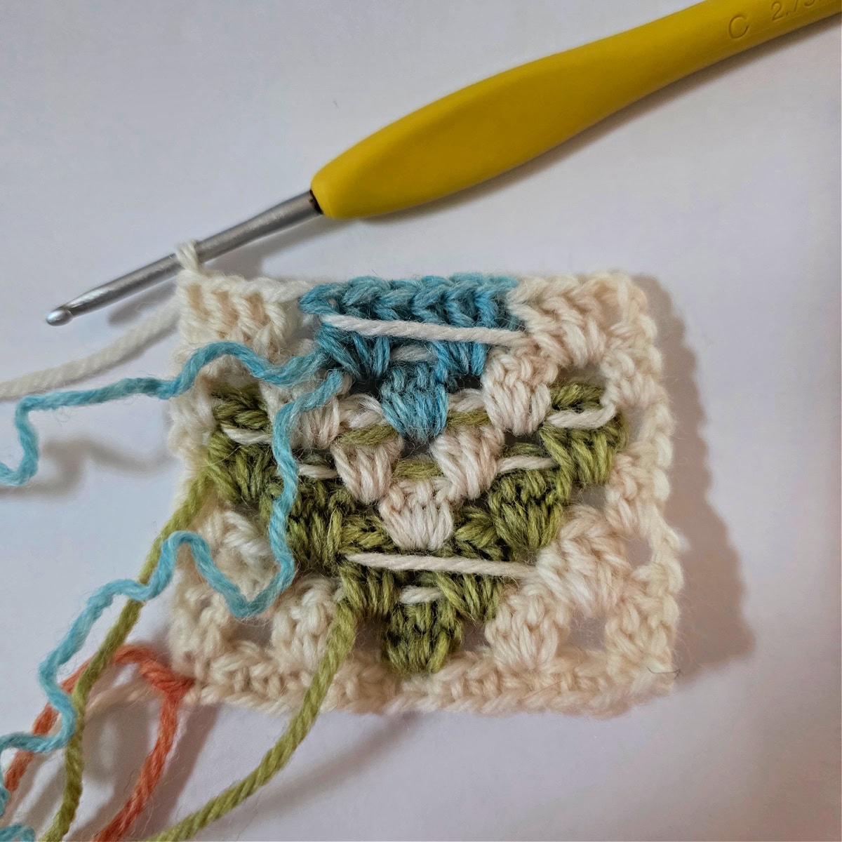 A granny stitch diamond in process on a small cream and aqua swatch.